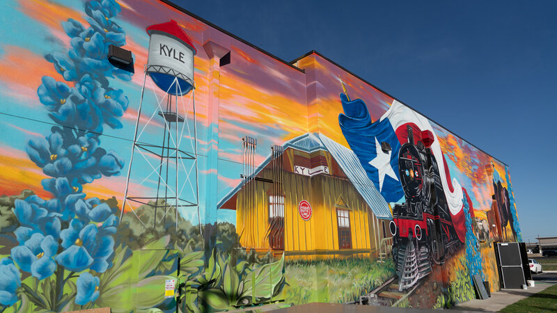 Colorful Kyle, Texas mural featuring water tower, train depot, bluebonnets, and Texas flag